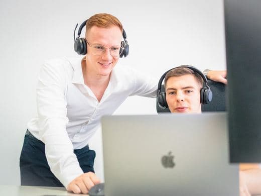 Zwei Mitarbeiter am Laptop, einer mit Headset