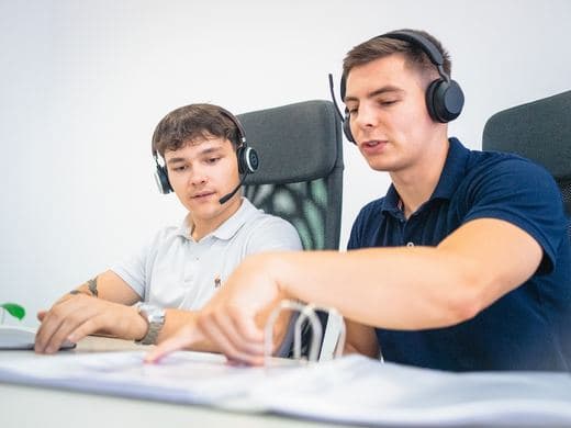 Zwei Mitarbeiter mit Headsets nebeneinander am Schreibtisch