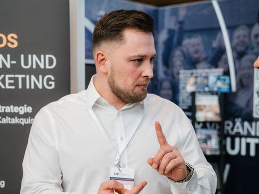 Mitarbeiter im Gespräch vor dem Messebanner der Agentur